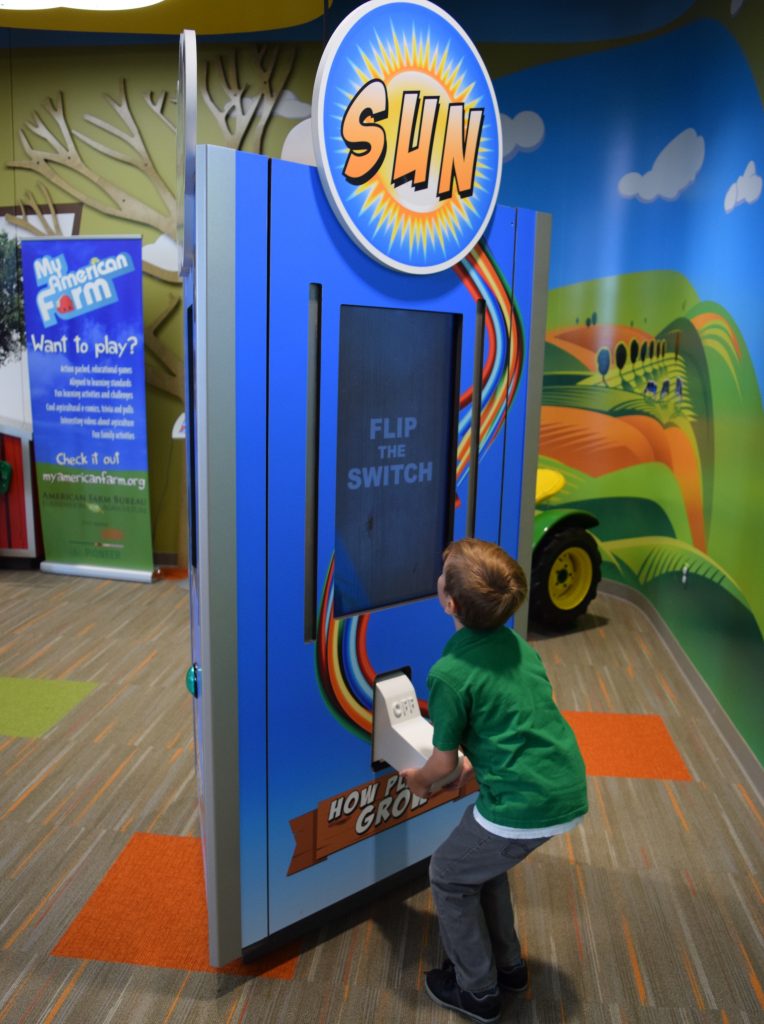 Boy flips a switch on the "How Plants Grow" kiosk.