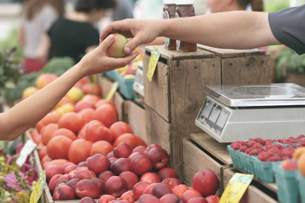 Seller handing apple to buyer at farmer's market; used for article on local food