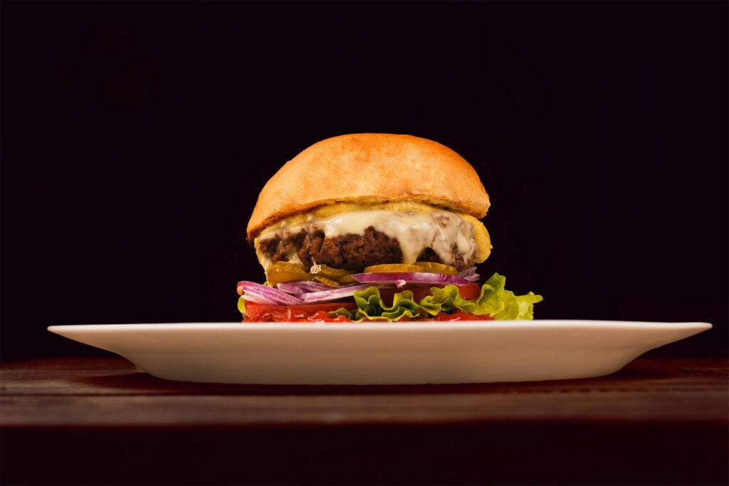 Fancy cheeseburger on a white plate against black background