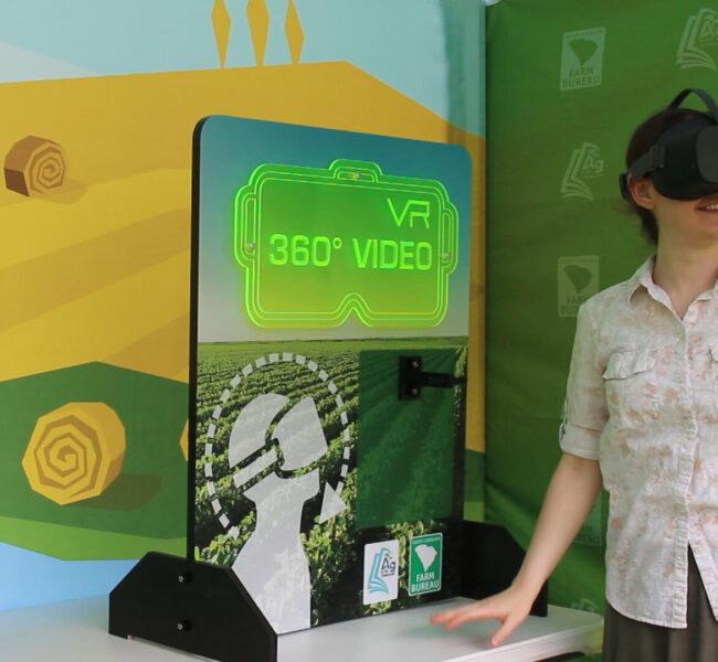 A woman standing next to the virtual reality station smiling while looking through VR goggles