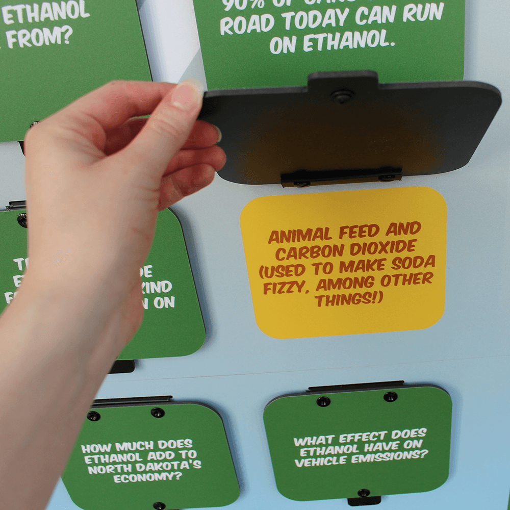 Hand lifting a flip-up door on the renewable fuels standup to show answer to trivia question