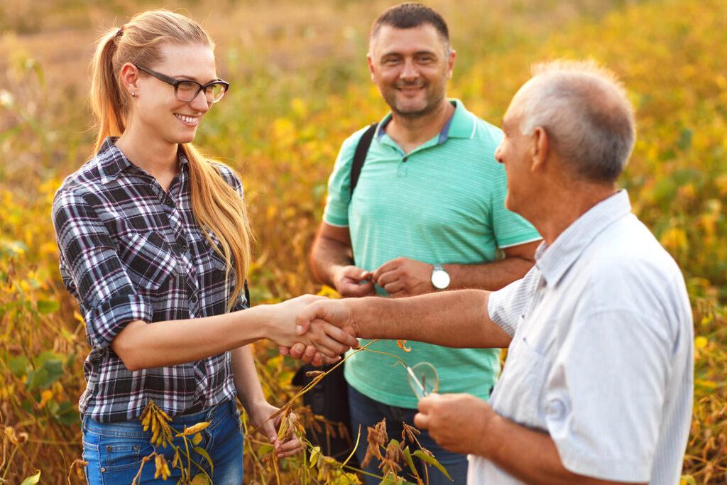 Young woman shaking hands with old man in soybean field