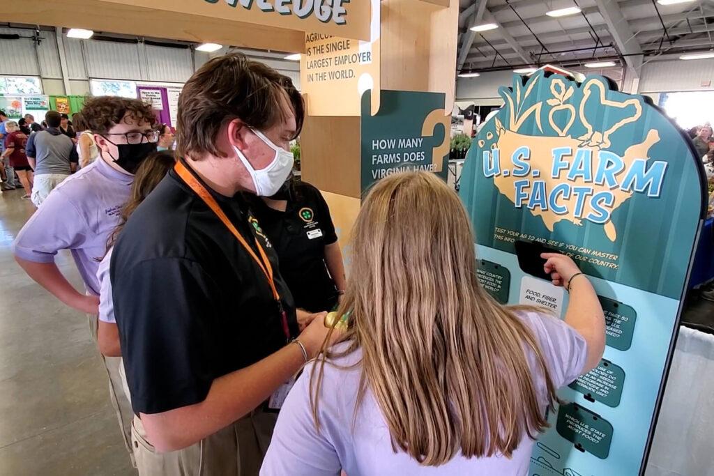 3 teenagers interact with a standup display for ag education at a state fair.