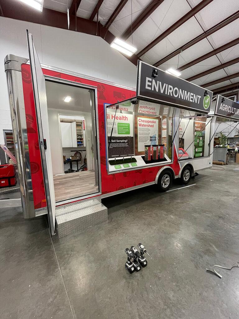 A red exhibit trailer with two exhibit windows open.